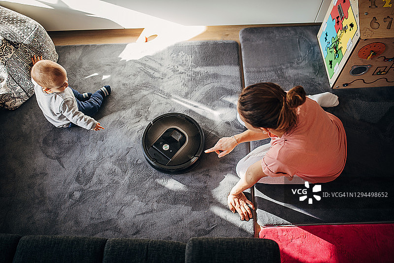 机器人吸尘器清洁地板，母亲和婴儿坐在地板上图片素材