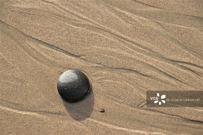 日落时分，在加利福尼亚州马里布，退潮时，一块孤独的圆形岩石躺在沙滩上图片素材