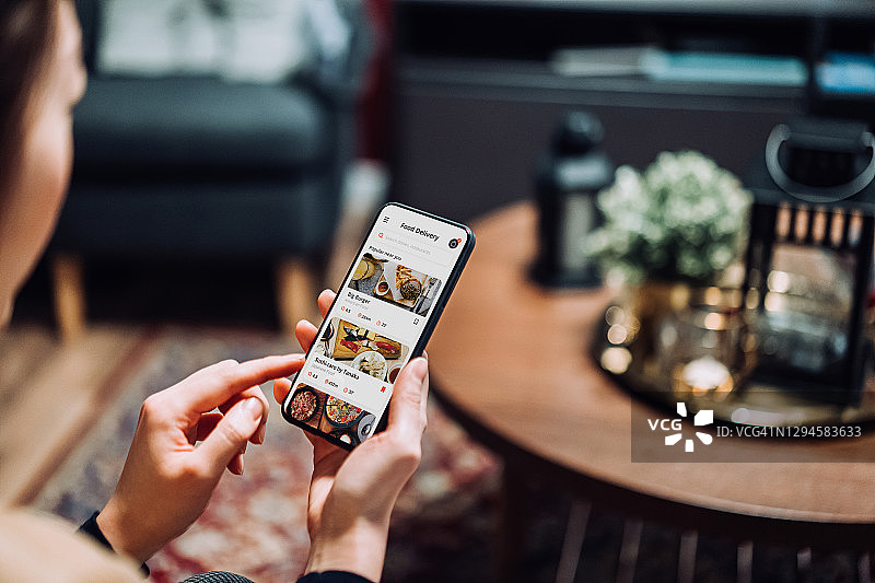 年轻的亚洲女性在舒适的家中沙发上使用送餐服务和通过手机App在线订购食物特写图片素材