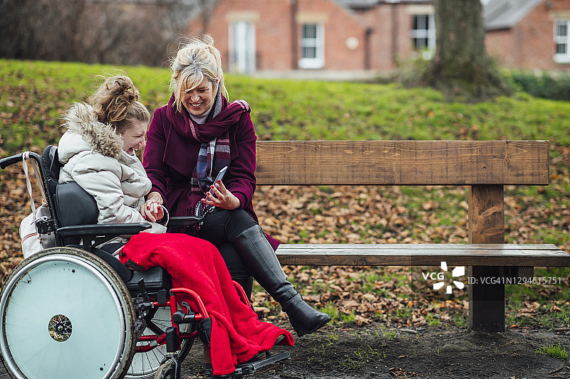 在公园长椅上使用智能手机的母女图片素材