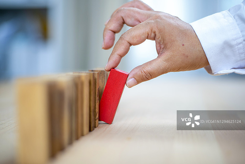 男人拿起红色木块，木块产生多米诺效应图片素材