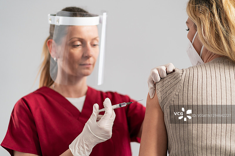 医生戴着防护面罩和外科手套，为患者手臂注射新冠疫苗图片素材