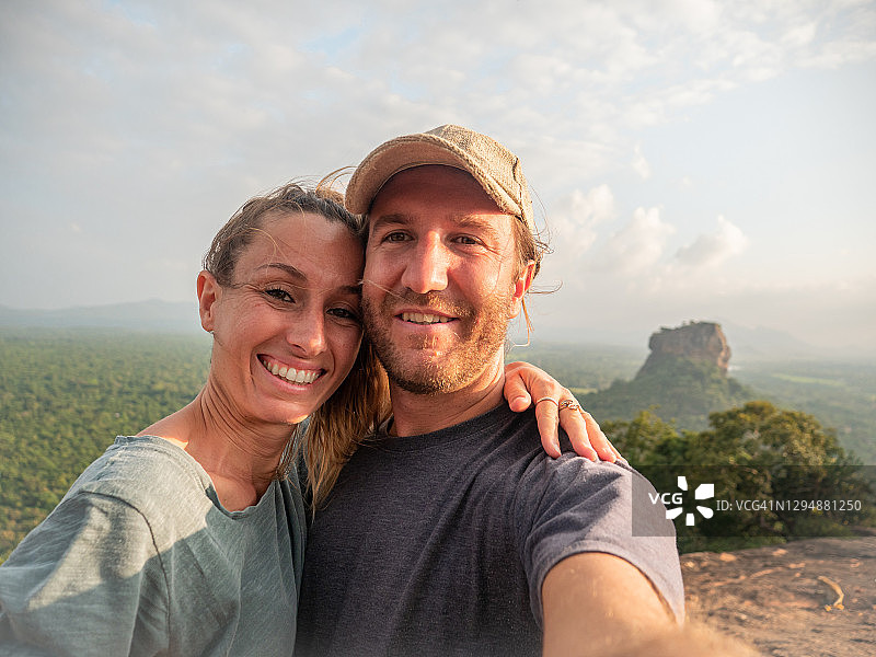 年轻情侣在日落时分在岩石顶上用手机自拍图片素材