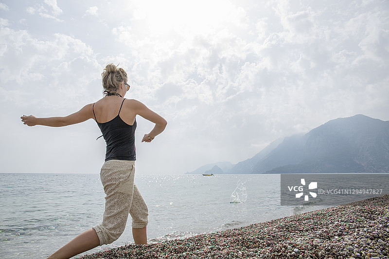 清晨，年轻女子在海滩上打水漂图片素材