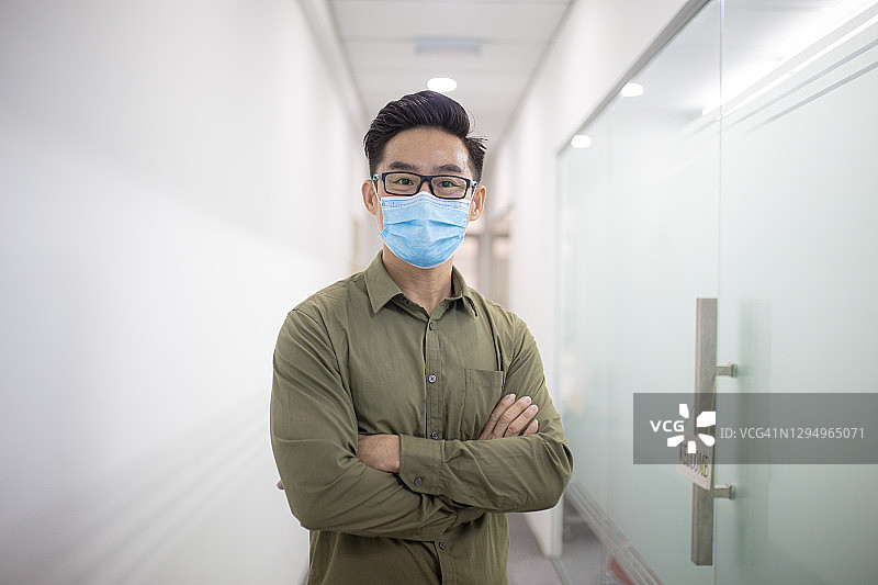佩戴口罩的亚洲华人商务人士在办公室走廊微笑图片素材