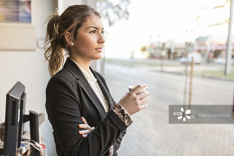 女办公室职员在办公室窗边喝咖啡，看着街景图片素材