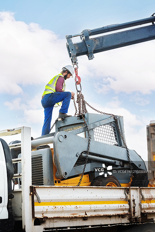 工人将链条绑在小型装载机上以便卸货图片素材