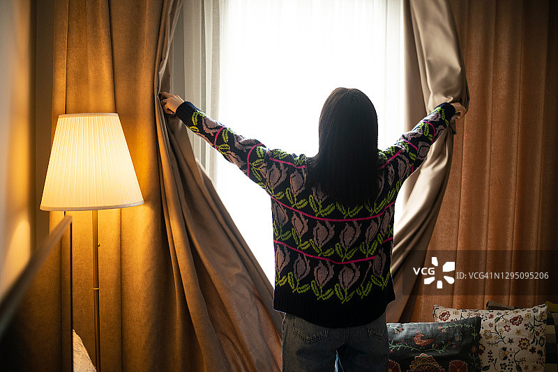早安！女人在客厅里打开窗帘图片素材