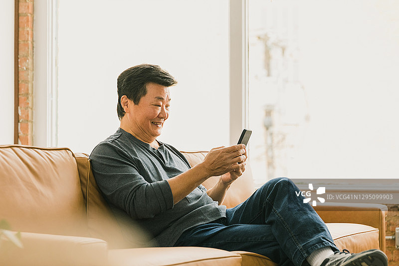 微笑的老年男人在家放松时使用智能手机图片素材