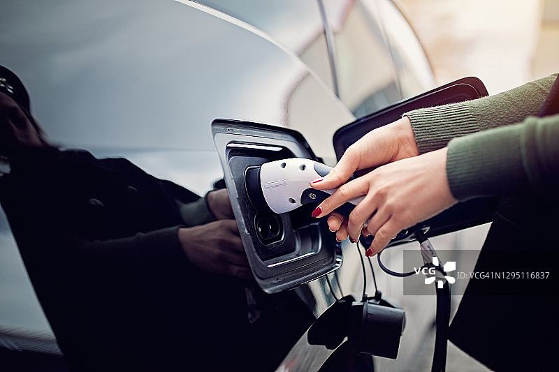 女人正在将电缆插入/拔出电动汽车图片素材