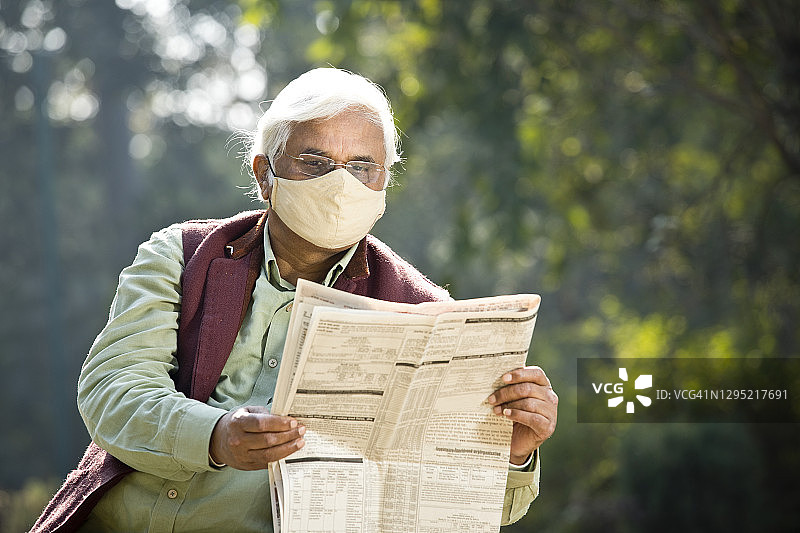 戴防护口罩看报纸的年长男人图片素材