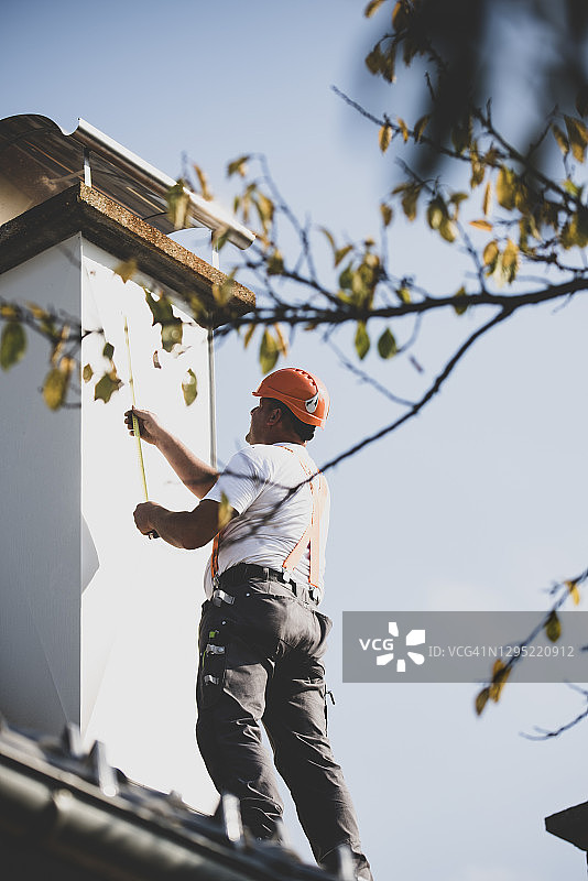 屋顶工人测量屋顶上的烟囱图片素材