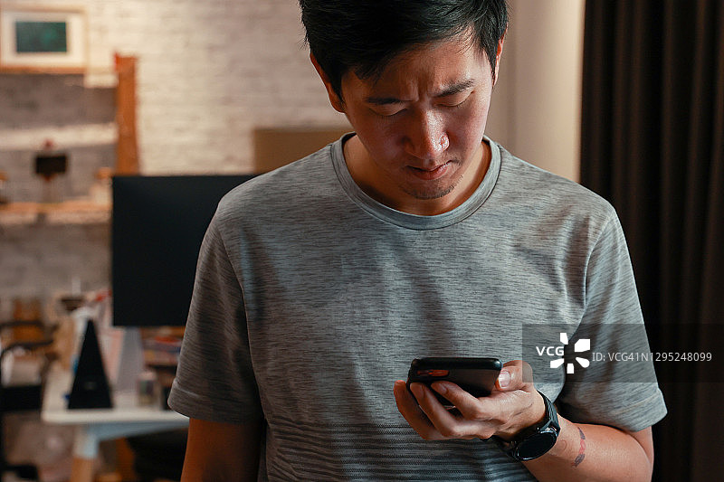 表情沮丧和担心的亚洲青年男子使用手机，带文案空间图片素材
