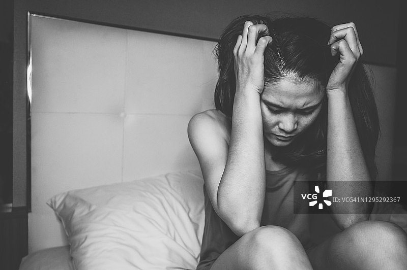 单色调：独自坐在卧室床上，情绪低落/有压力的女人肖像图片素材