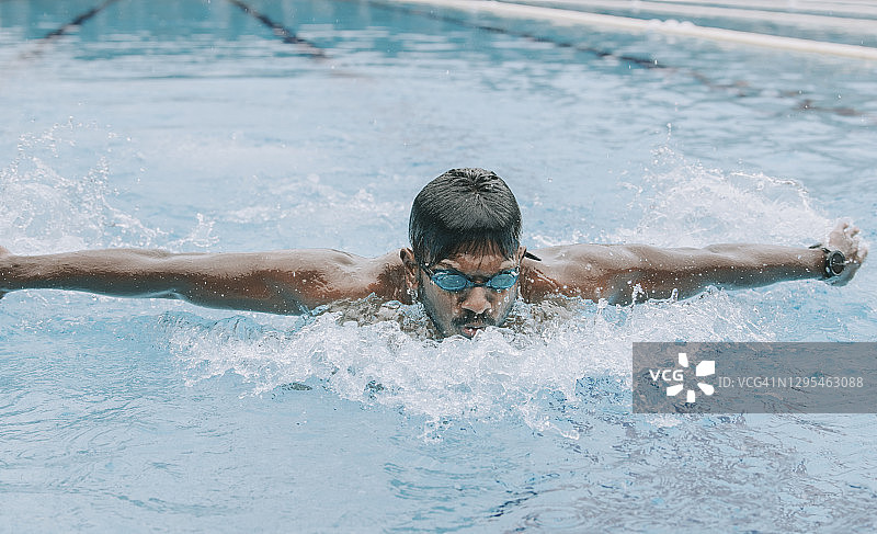 亚洲印度裔游泳运动员在游泳池里游泳和练习蝶泳图片素材
