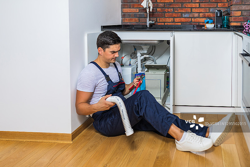 水管工在厨房水槽下进行维修图片素材
