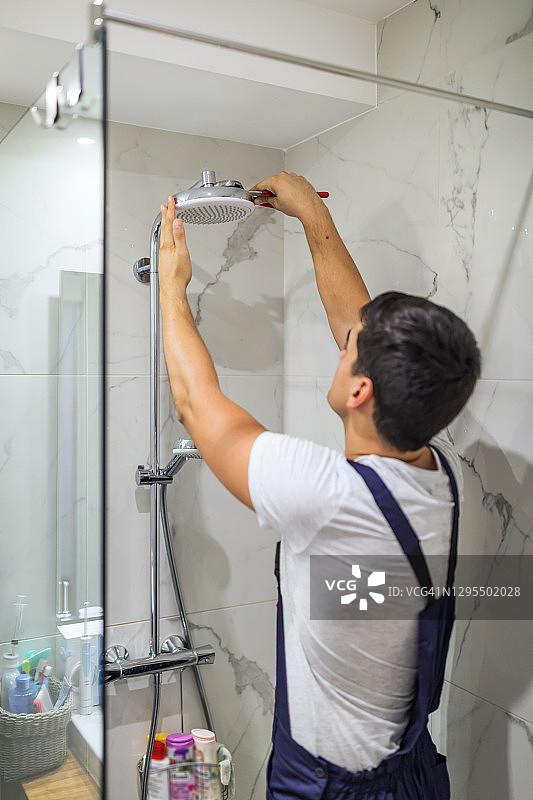 更换浴室中的管道，安装可调节高度的手持花洒支架图片素材