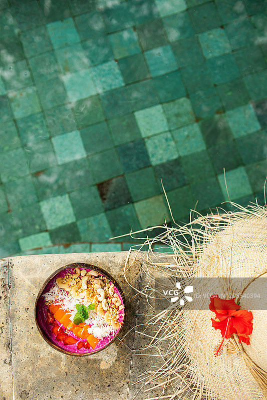 新鲜热带有机水果冰沙，椰子碗配吸管，亚洲度假村泳池边的夏日草帽。火龙果和香蕉纯素碗，配木瓜、谷物坚果和种子。夏日氛围。图片素材