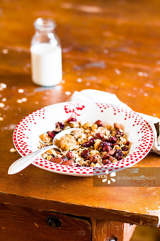 一盘健康的自制格兰诺拉麦片或混合麦片，配烤燕麦片、干梨、榛子，搭配一瓶新鲜牛奶，木桌上，选择性聚焦。图片素材