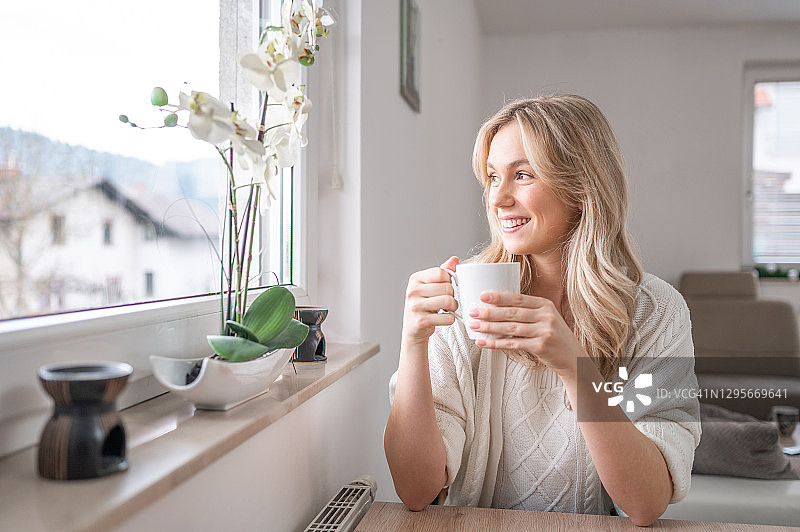 年轻女人手拿咖啡杯望向窗外图片素材
