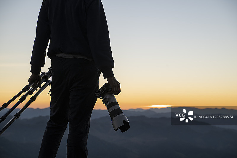 摄影师手持相机和三脚架的背面图片素材