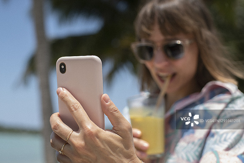 女人在沙滩上使用智能手机喝鸡尾酒图片素材