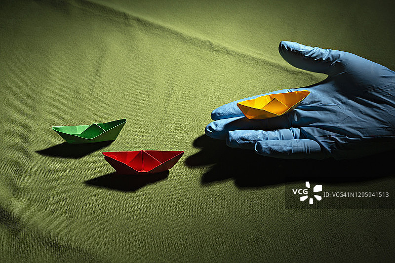 戴防护手套的手拿着折纸船图片素材