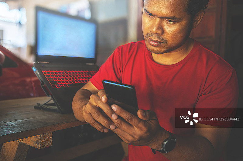 亚洲男人坐在室内桌旁，神情严肃地看着智能手机图片素材