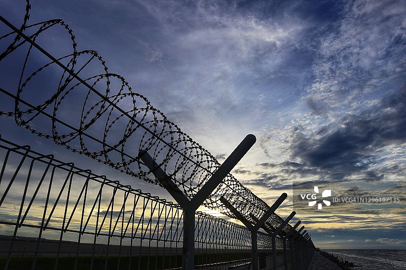 日落天空背景下的带刺铁丝网图片素材