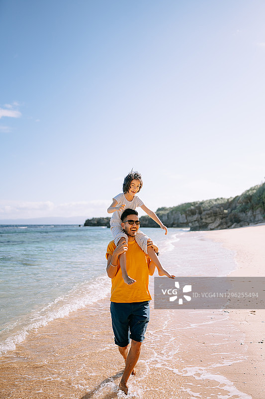 父亲在热带海滩上肩上扛着女儿图片素材