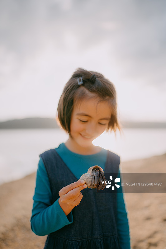 好奇的女孩在沙滩上拿着巨大的寄居蟹，日本图片素材