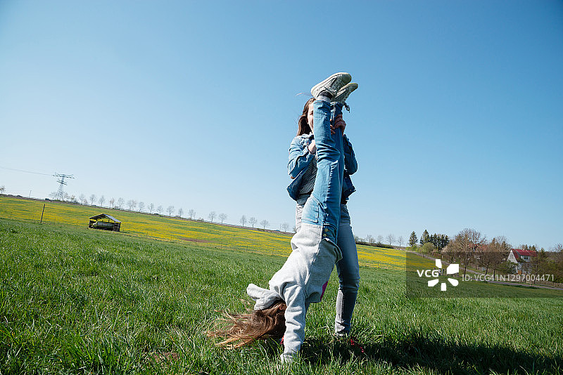 快乐的女孩们在夏日草地上尝试倒立图片素材