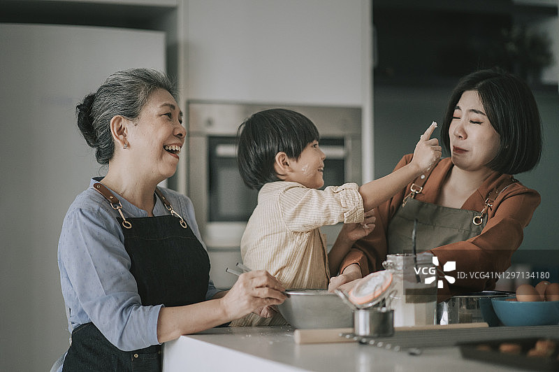 中国男孩在厨房和母亲、祖母一起烘焙时，用面粉触摸母亲的鼻子图片素材