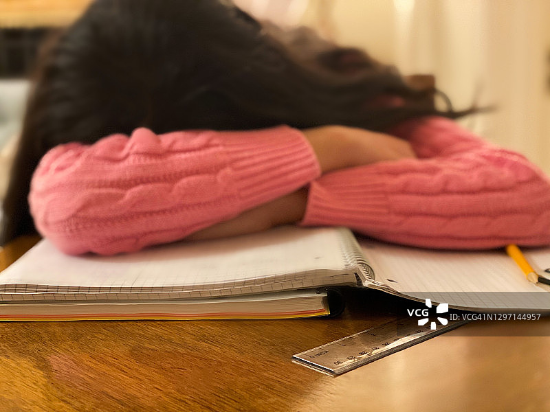 混血少女坐在书桌前，头靠在笔记本上休息图片素材