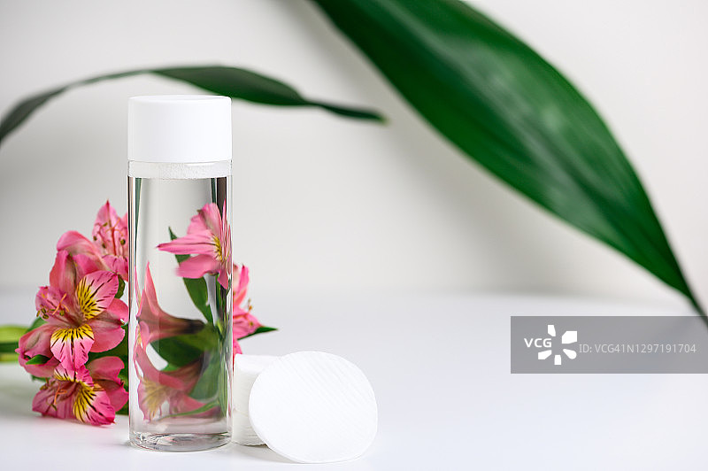 透明的天然胶束水和化妆棉，配以鲜花和绿叶，用于清洁和清新肌肤的卸妆液，塑料包装图片素材