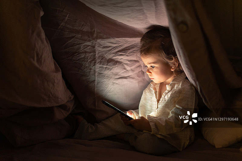夜晚在床上看智能手机的女婴图片素材