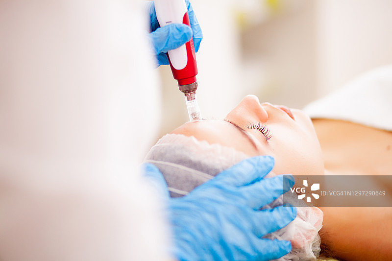 美容师在美容院为一位美丽的年轻女子做面部微晶磨皮护理图片素材