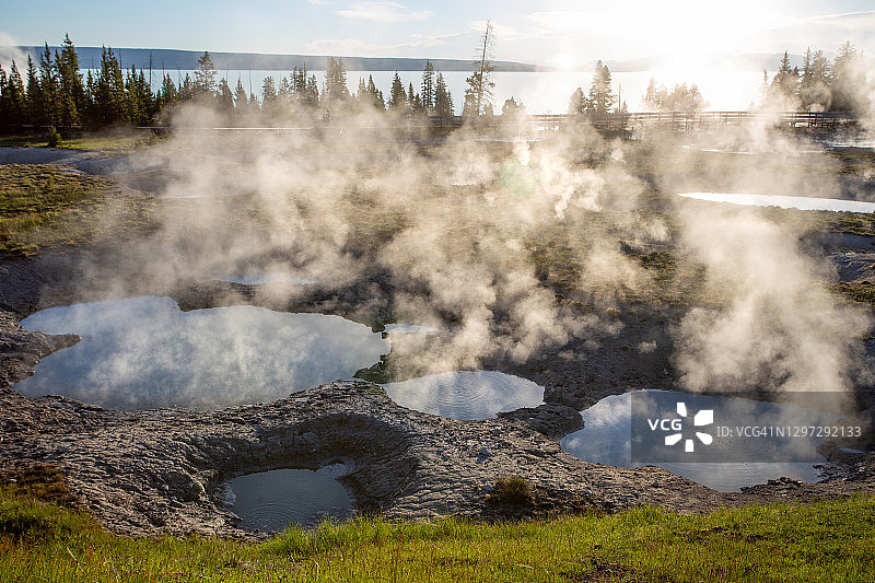 西拇指间歇泉盆地，黄石湖附近森林中日出时蒸汽腾腾的地热池的广角镜头图片素材