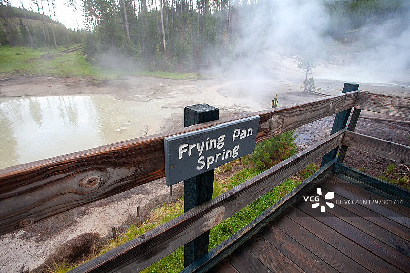 在木板路栏杆上的煎锅泉标志和背景中的地热池的POV视角图片素材