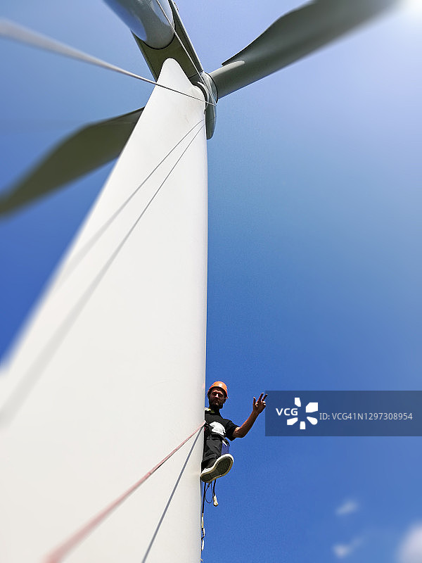 仰视角度拍摄的工业攀爬者在巨大的陆上风力涡轮机叶片上工作并做出胜利姿势图片素材