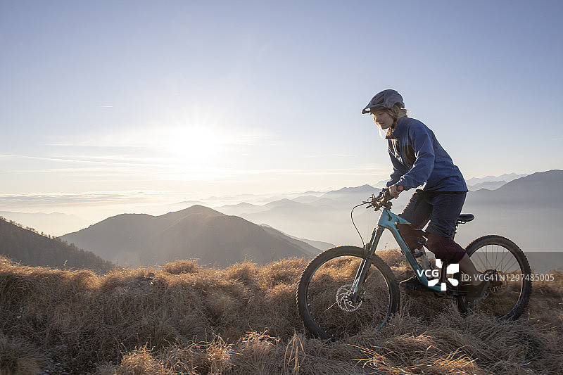 骑山地自行车的女人在日出时沿着山脊骑行图片素材