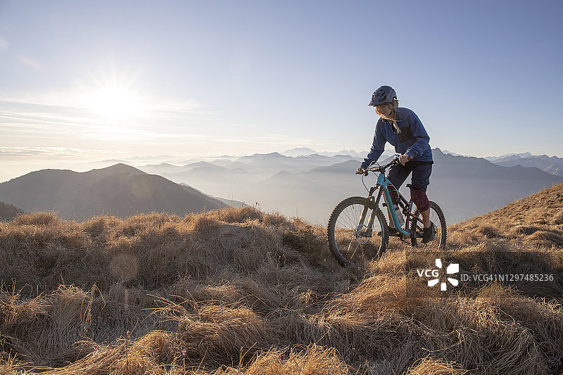 骑山地自行车的女人在日出时沿着山脊骑行图片素材