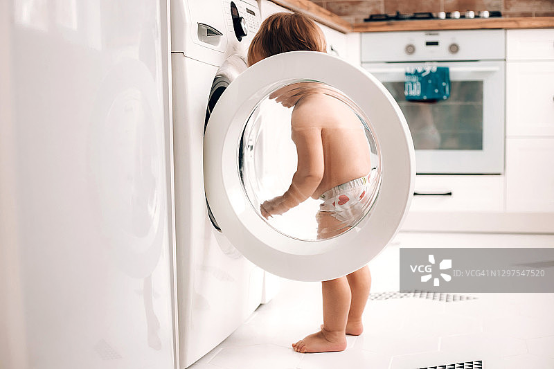 站在厨房洗衣机旁的可爱婴儿图片素材