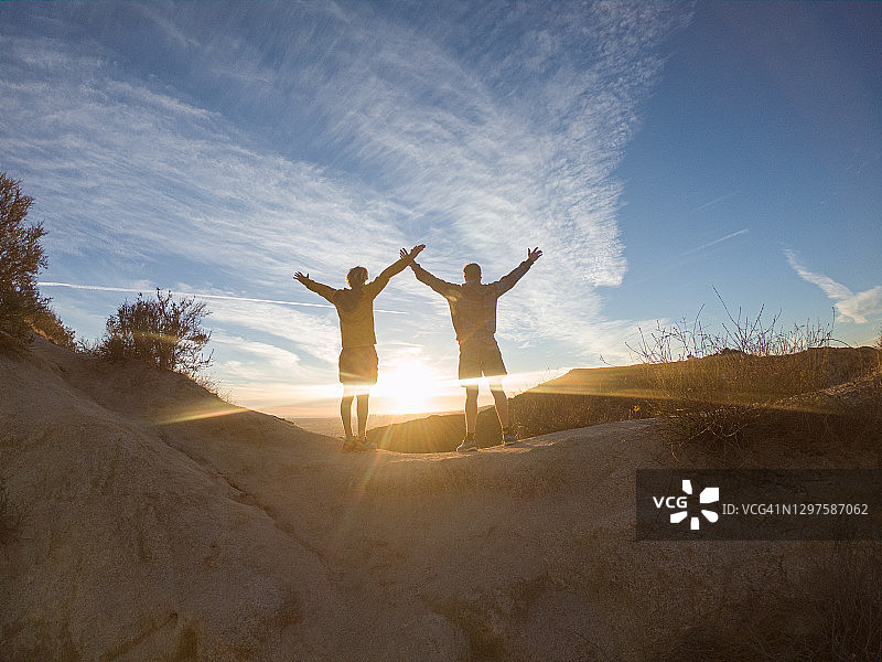 两个男人站在岩石顶上，日落时张开双臂图片素材