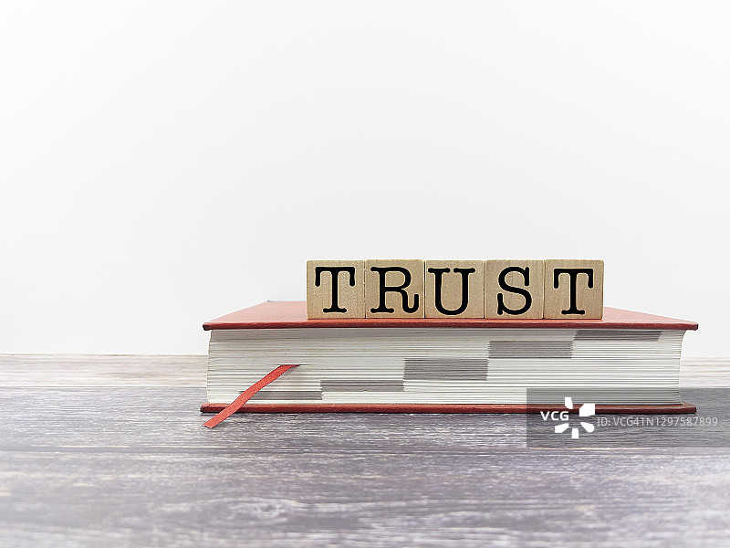 木块上的“信任”字样与红色封面书籍，构建信任商业理念图片素材