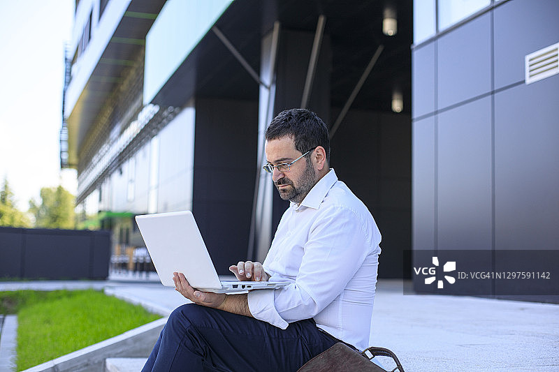 在公司大楼前使用笔记本电脑的经理图片素材