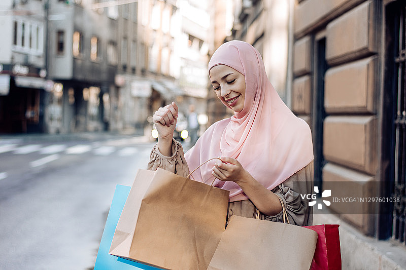 看着购物袋、心情愉悦的漂亮穆斯林女人图片素材