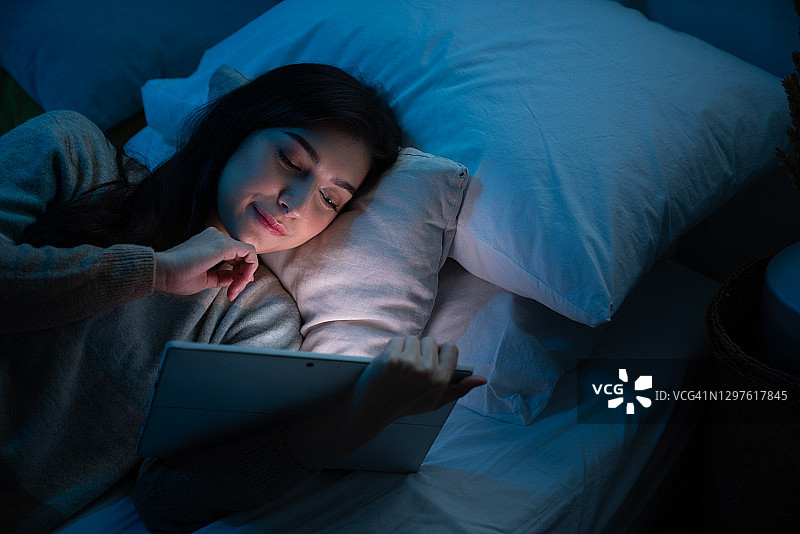 深夜躺在床上，使用智能手机查找社交媒体的女人，沉迷于互联网图片素材