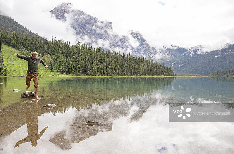 在阿尔卑斯湖泊中跳跃于岩石之间的男性徒步者图片素材