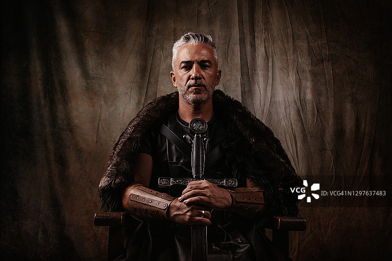 维京风格的强大奇幻骑士坐在简单的木制宝座上看镜头图片素材